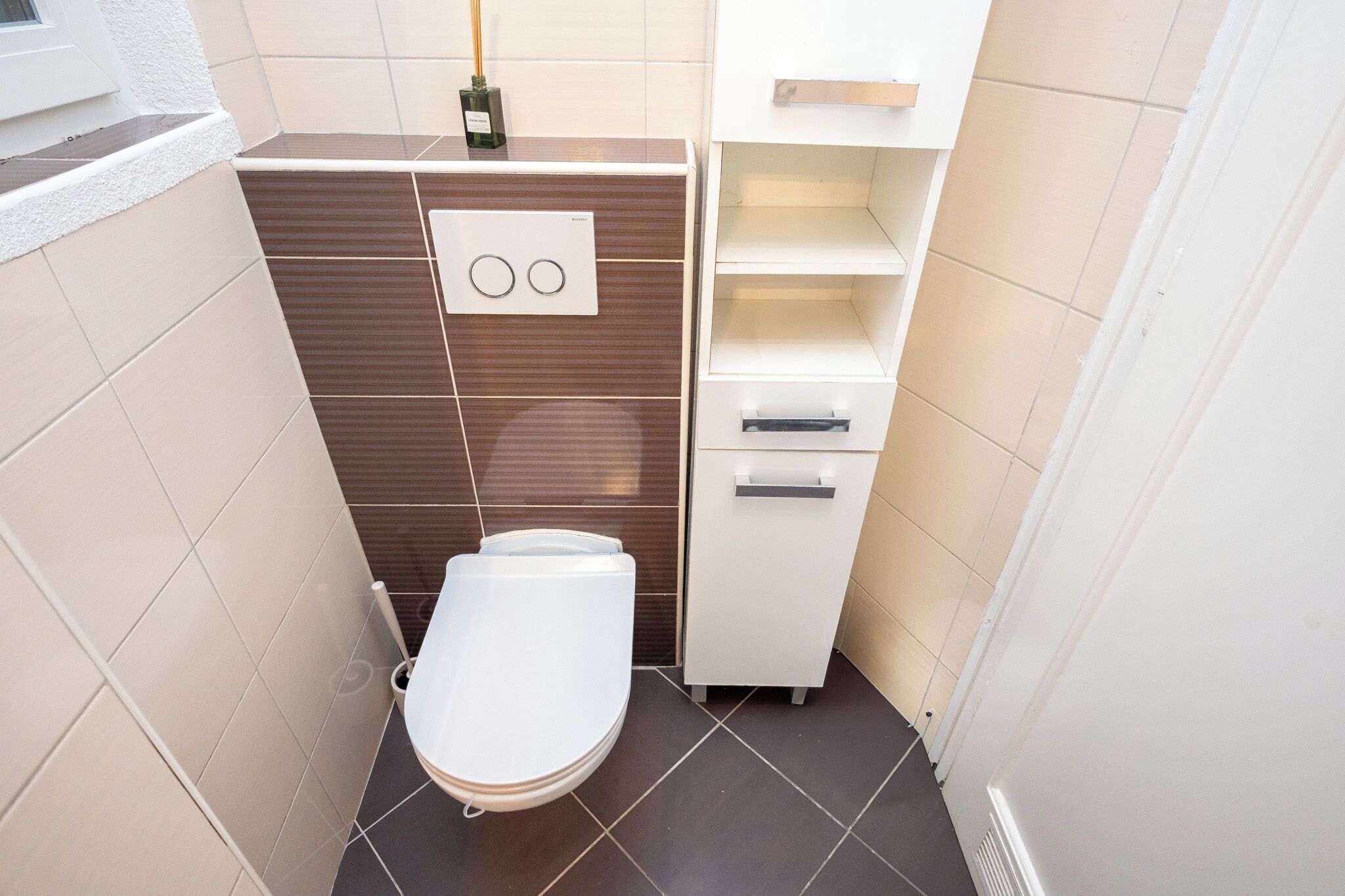 A small bathroom with a toilet, a cabinet with drawers, and a shelf unit.