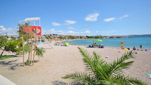 A beach with a lifeguard tower, umbrellas, and people relaxing. - House Kreso (Sibenik)