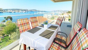 Un balcon avec une table et des chaises, donnant sur une marina où sont amarrés des bateaux, et sur une vue lointaine de la ville.