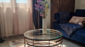 Una sala de estar con una mesa de centro redonda de vidrio, un sofá azul y un armario de madera.