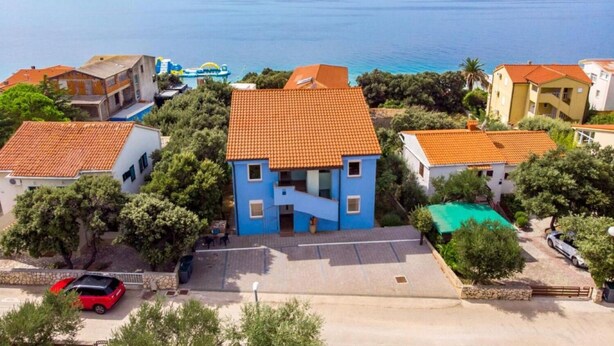 Un quartier résidentiel situé sur la côte, avec des maisons dotées de toits recouverts de tuiles rouges et un bâtiment central de couleur bleue, agrémenté d’un escalier.