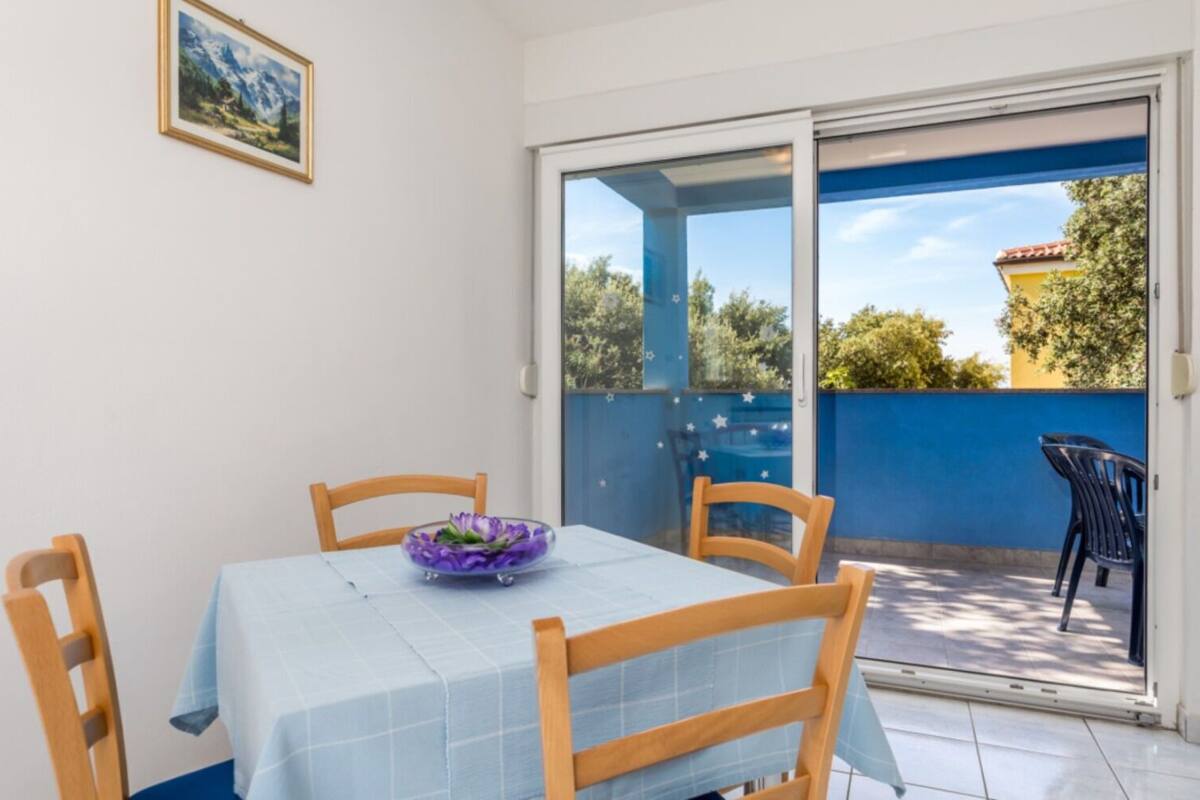 Un coin repas avec une table dressée pour deux personnes, une nappe bleue et un bol violet posé sur la table.