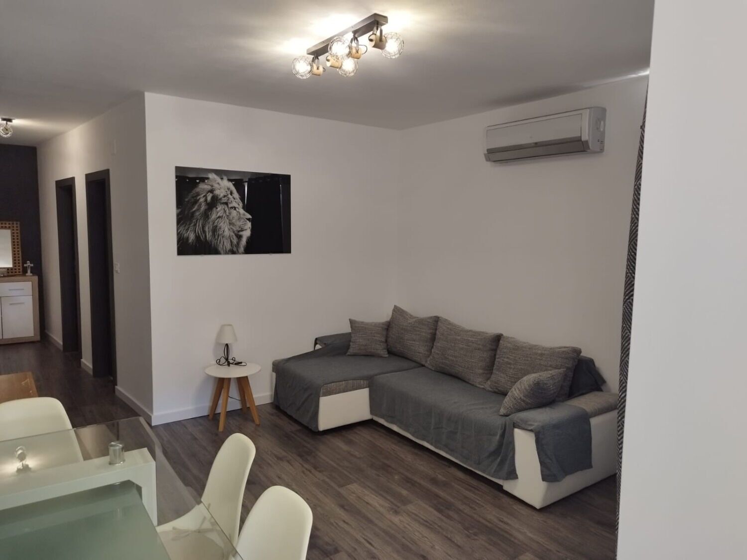 Una sala de estar moderna con un sofá seccional, un comedor con una mesa de vidrio y un aire acondicionado instalado.