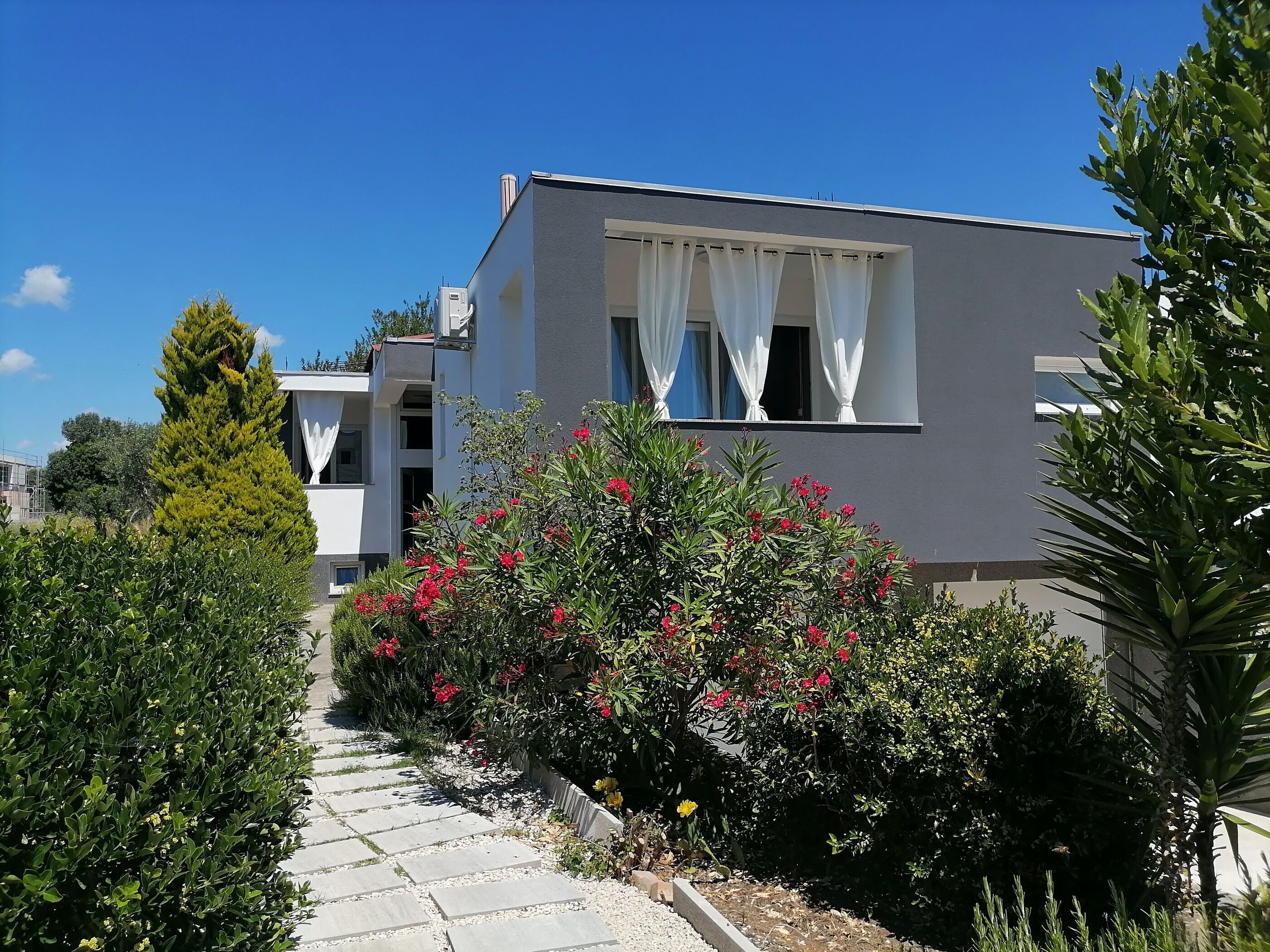 Un bâtiment moderne doté d’un toit plat, de murs extérieurs blancs et d’un balcon agrémenté de rideaux blancs.