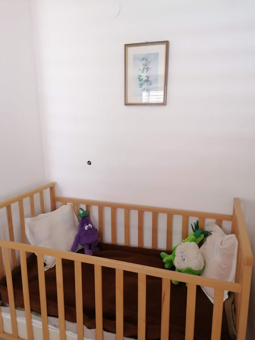 Una cuna de madera con un colchón marrón, un juguete de peluche morado y un juguete de peluche verde.