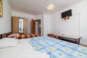 A bedroom with a bed, a bench, a television mounted on the wall, and a door leading to another room. - Apartments Olgi (Crikvenica)
