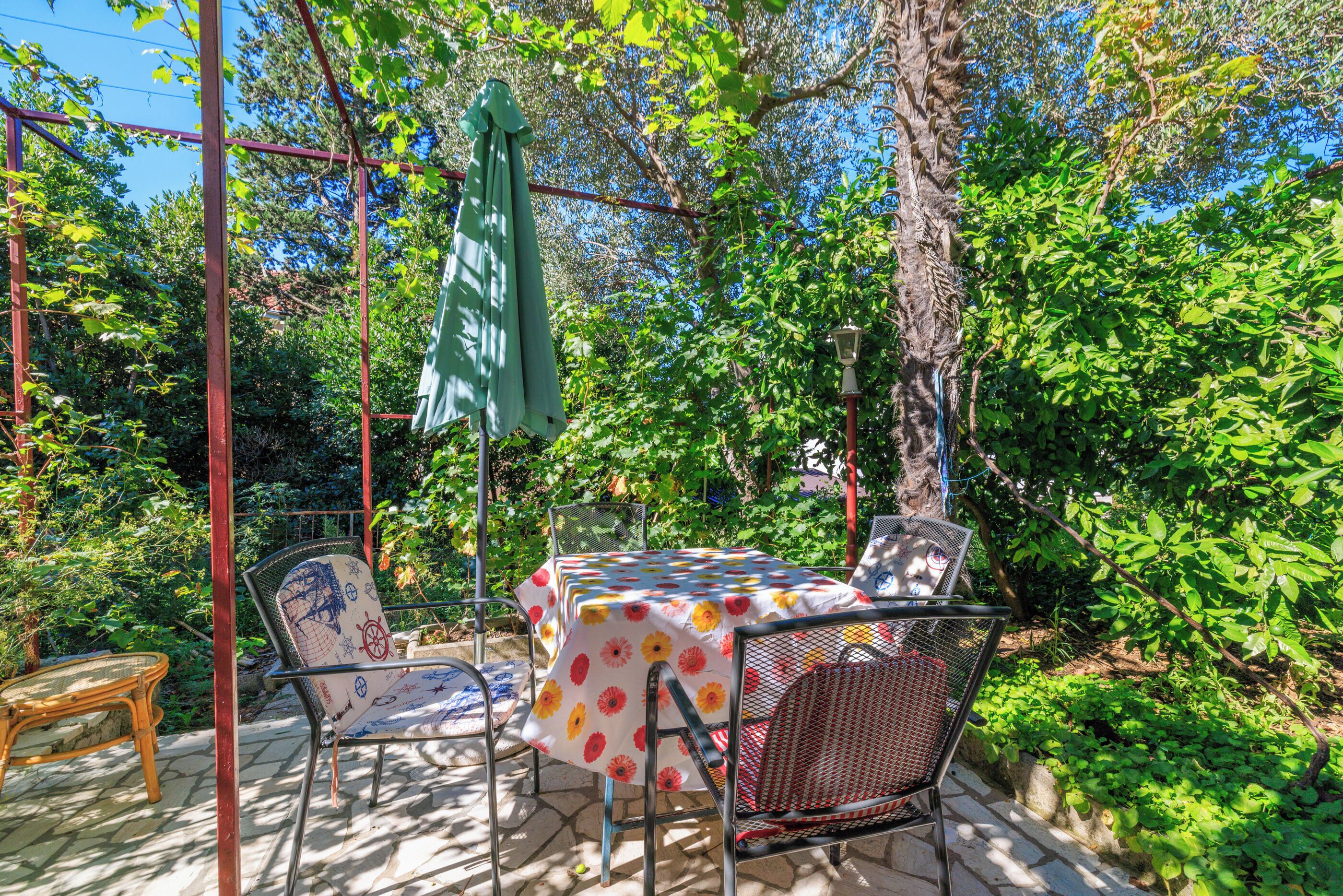 Eine Terrasse im Freien mit Tisch und Stühlen, umgeben von üppiger Bepflanzung und einer Pergola.