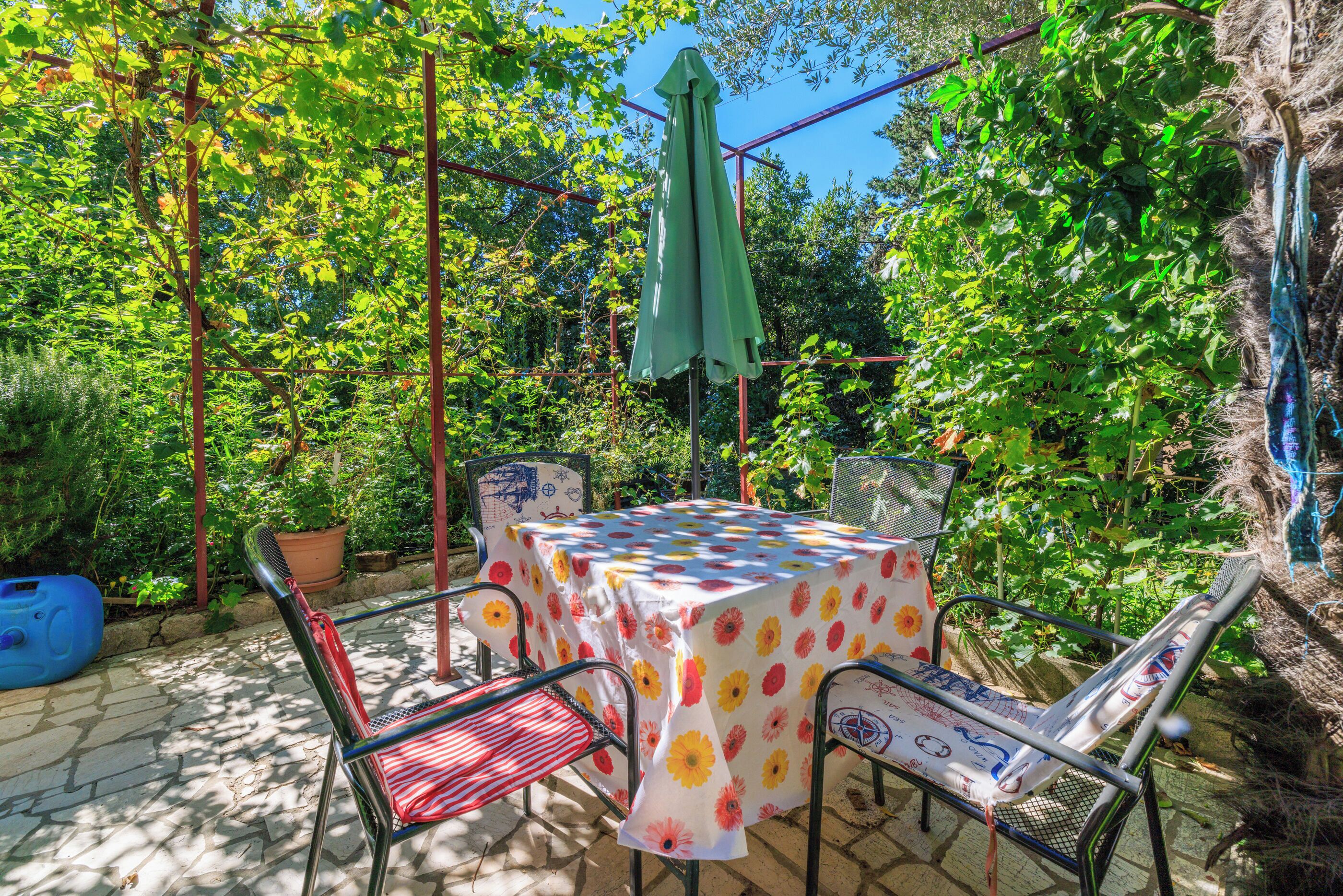 Een terras met een tafel bedekt met een bloemrijk tafelkleed, omringd door metalen stoelen en een parasol.