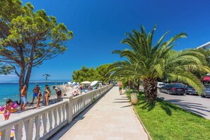 A coastal promenade with a clear view of the sea, palm trees, and a sidewalk lined with beachgoers. - Apartments Olgi (Crikvenica)