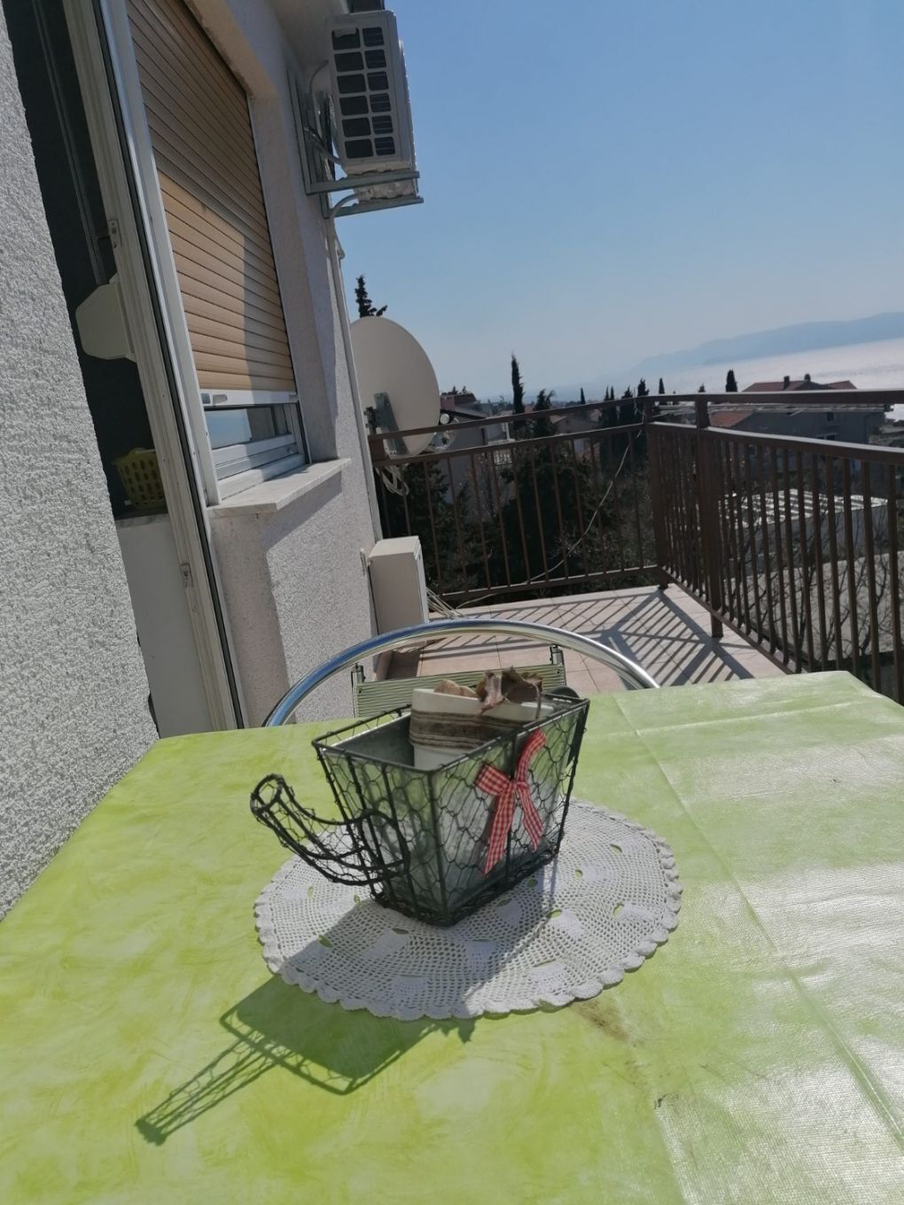 A balcony with a table, a metal basket, and a view of the cityscape.