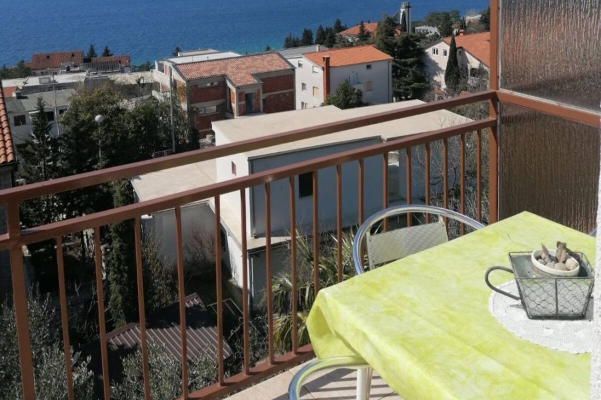 A balcony with a table and chairs, overlooking a coastal town and the sea.