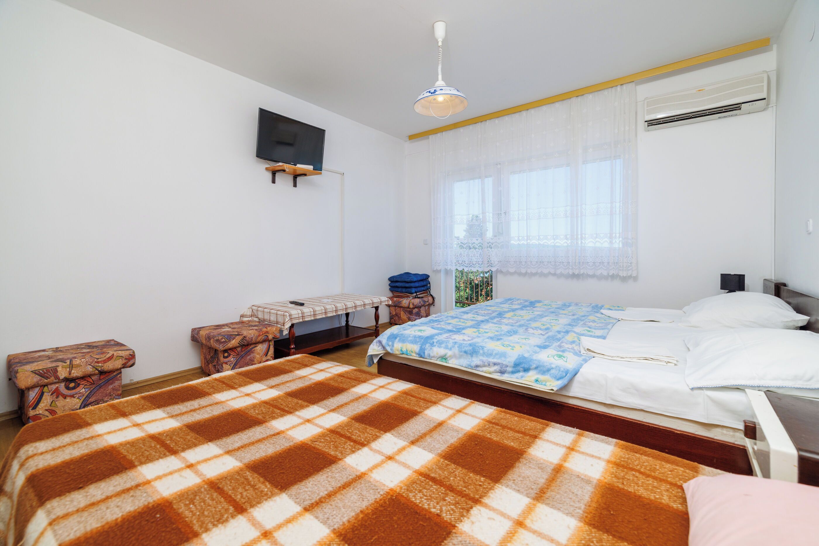 Une chambre à coucher comprenant un lit, une table de chevet, une chaise, un téléviseur fixé au mur et un appareil de climatisation.