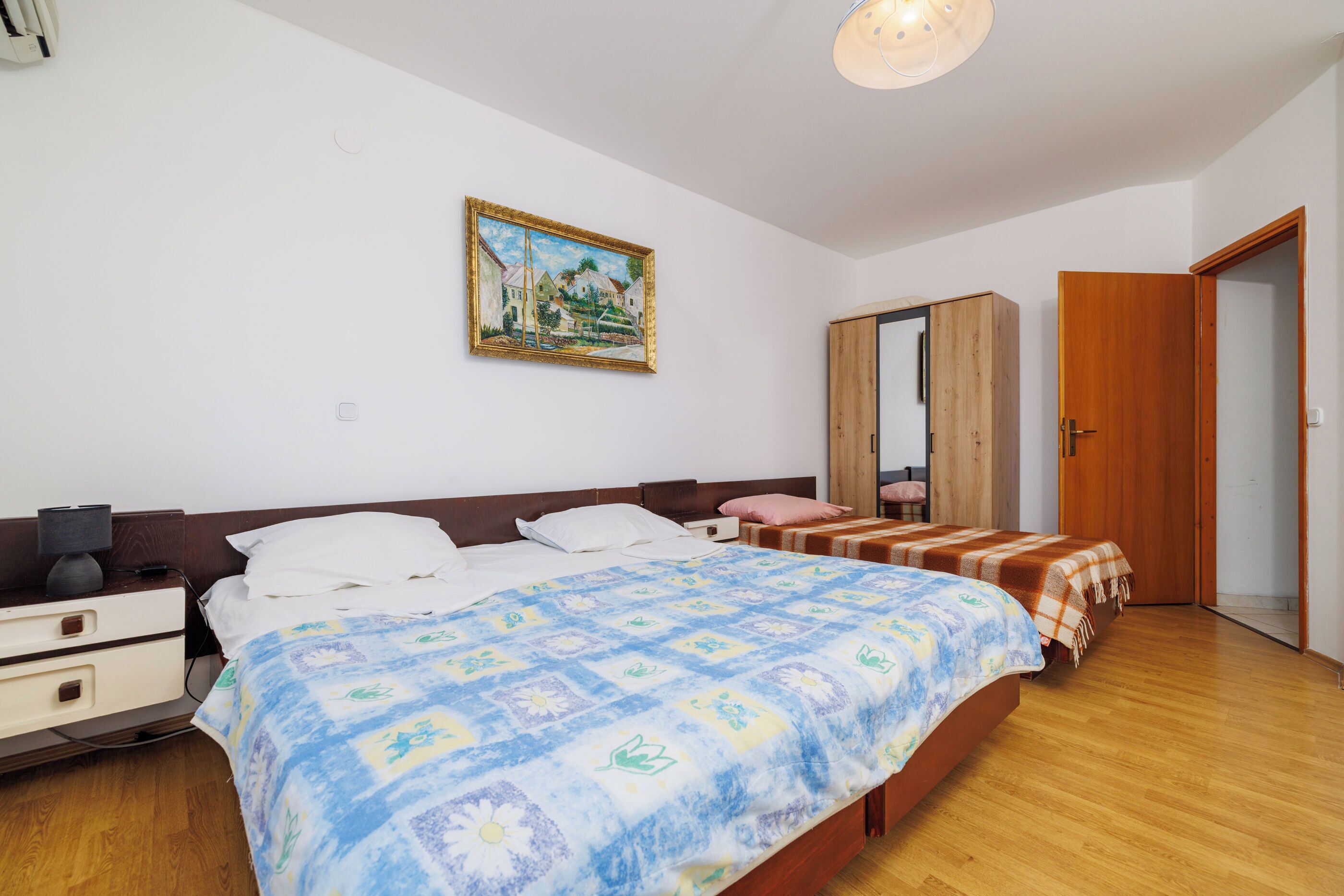A bedroom with a large bed, a dresser, a wardrobe, and a mirror.