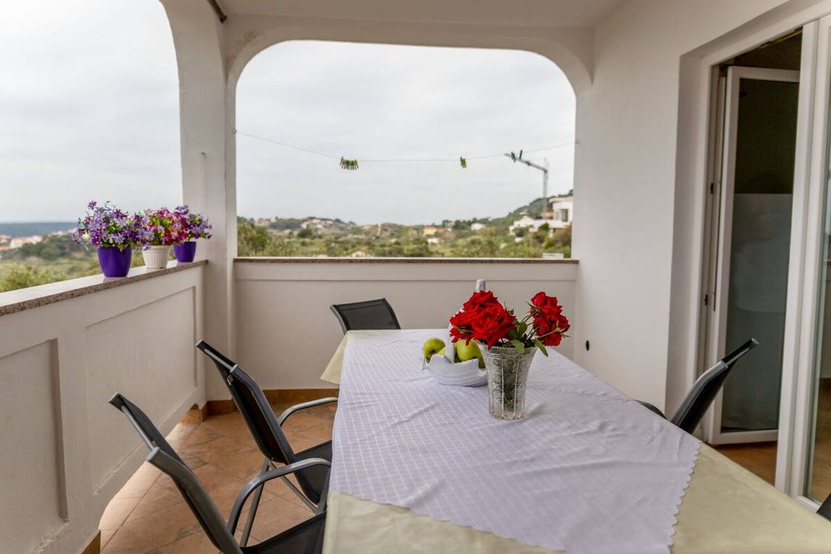 A balcony with a table set for two, chairs, and potted plants.
