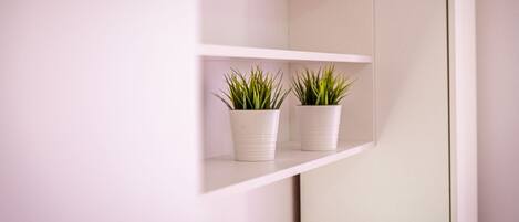 A white wall with a mirrored section and two white shelves holding potted plants.