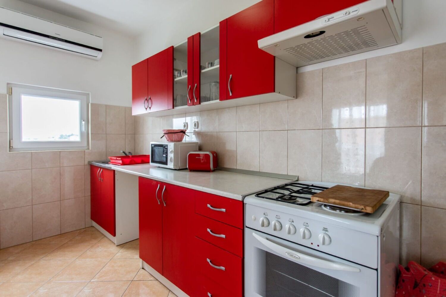 Une cuisine avec des meubles de rangement rouges, une cuisinière à gaz, un four à micro-ondes et un grille-pain.