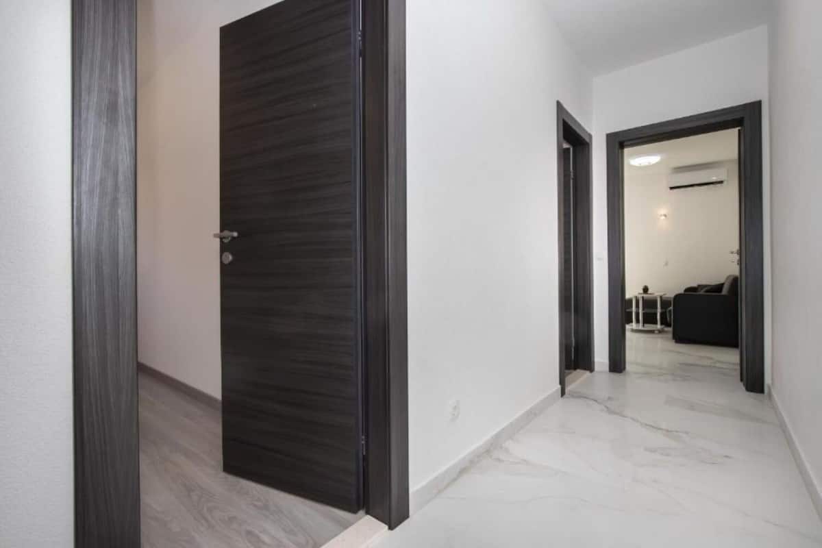 A hallway with a dark wooden door, white walls, and a marble floor.