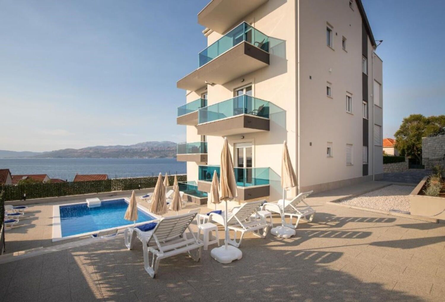 A modern building with a pool, sun loungers, and a view of the sea.