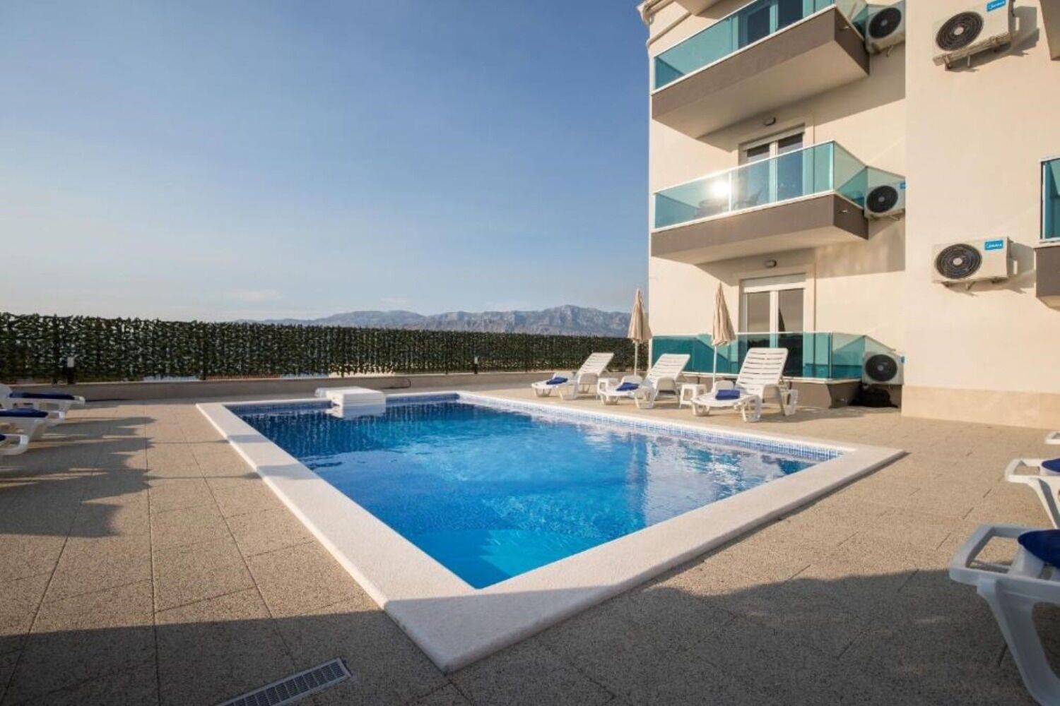 Une piscine sur le toit, dotée de chaises longues, offrant une vue dégagée sur les montagnes et équipée de climatiseurs installés sur le bâtiment.
