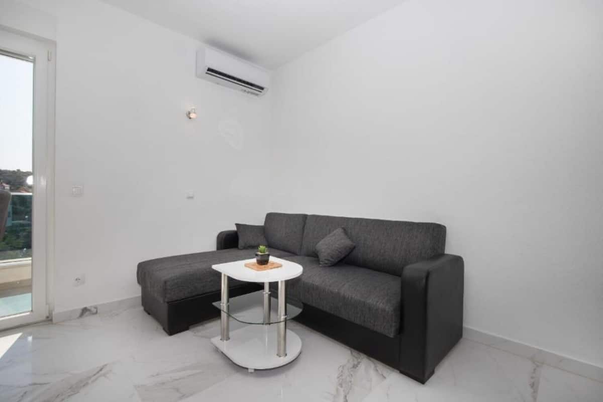 A modern living room with a grey sofa, a small white table with a plant, and a glass coffee table.