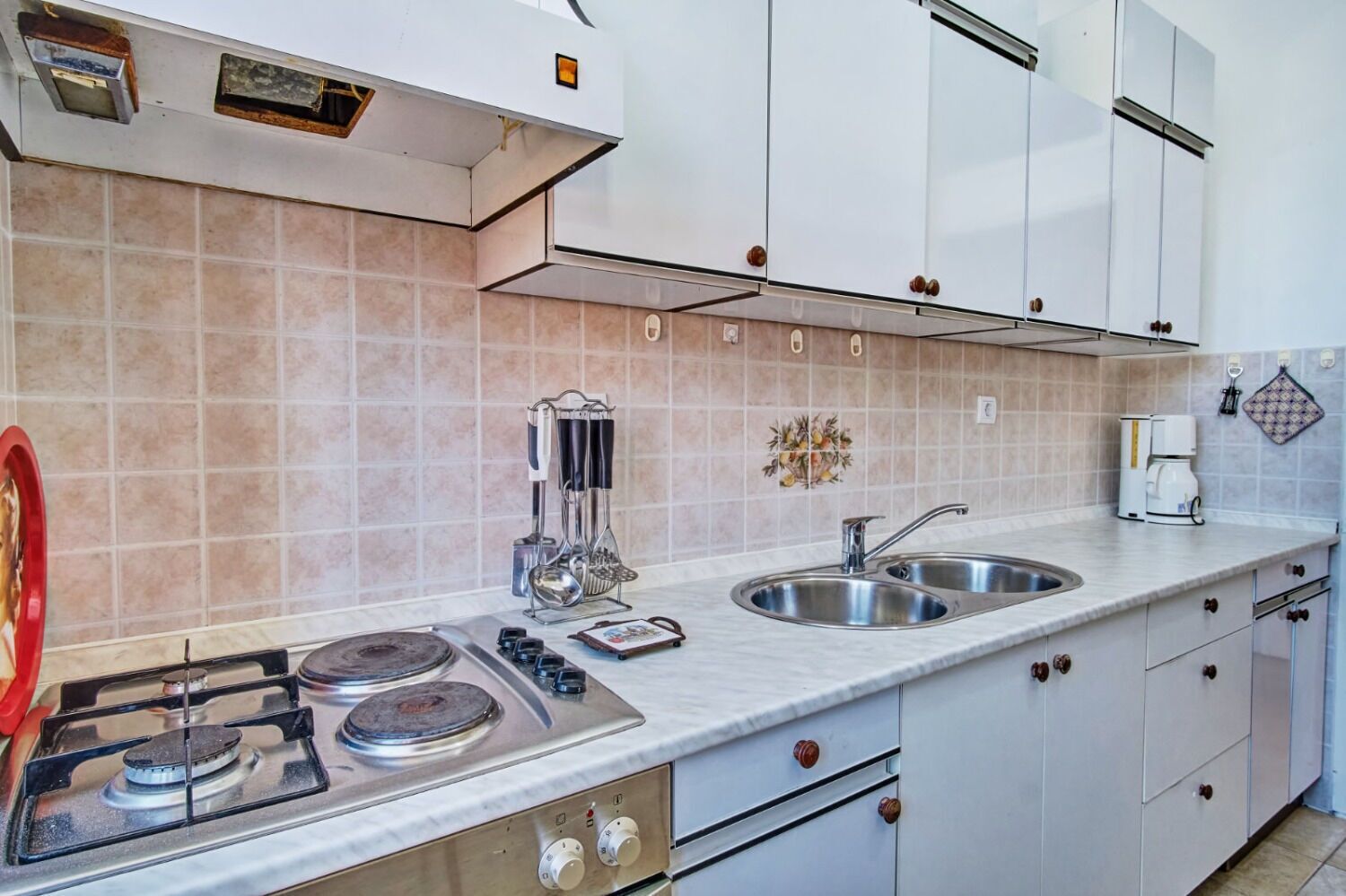 A modern kitchen with a gas stove, stainless steel sink, and white cabinets.