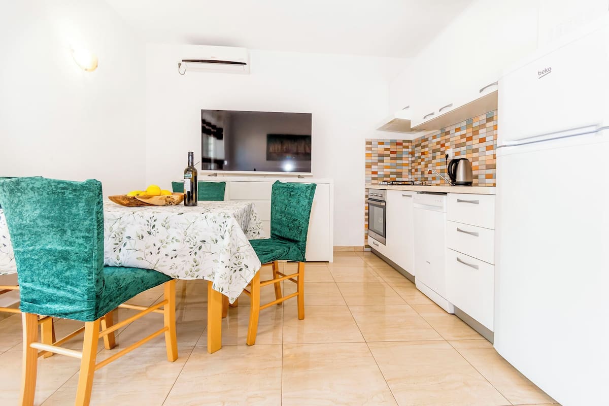 Une cuisine moderne avec des meubles blancs, un pare-feu en carreaux et un coin repas comprenant une table et des chaises.