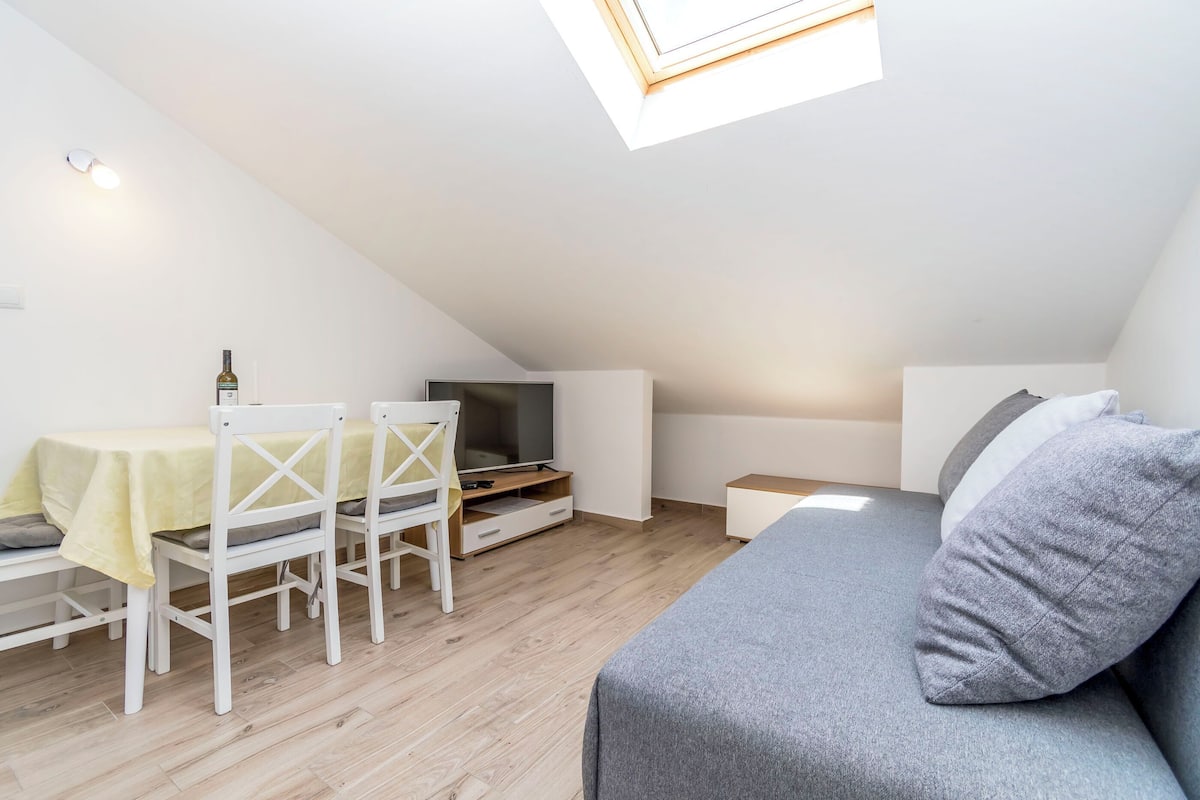 Une petite pièce moderne avec un lit en mezzanine, une télévision, une table à manger avec des chaises et une lucarne.