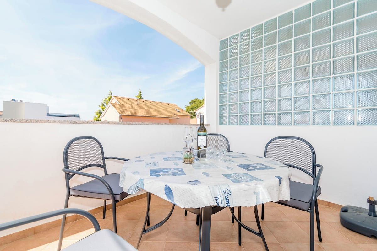 Un coin repas avec une table dressée pour quatre personnes, des chaises, une bouteille de vin et un pichet.