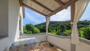 Un balcón con mesa y sillas, que ofrece vistas a un paisaje verde exuberante y colinas.
