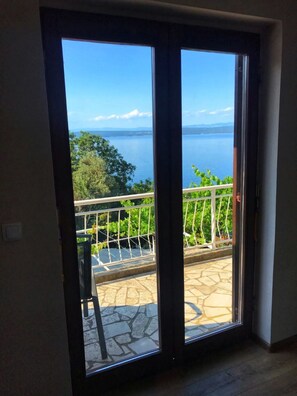 A room with a sliding glass door leading to a balcony with a stone floor and a metal railing. - Apartment Luki (Cres)