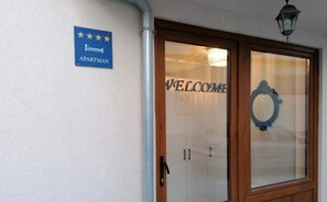 Entrada de un hotel con un cartel que indica que es un hotel-apartamento, un letrero de bienvenida y un candelabro.