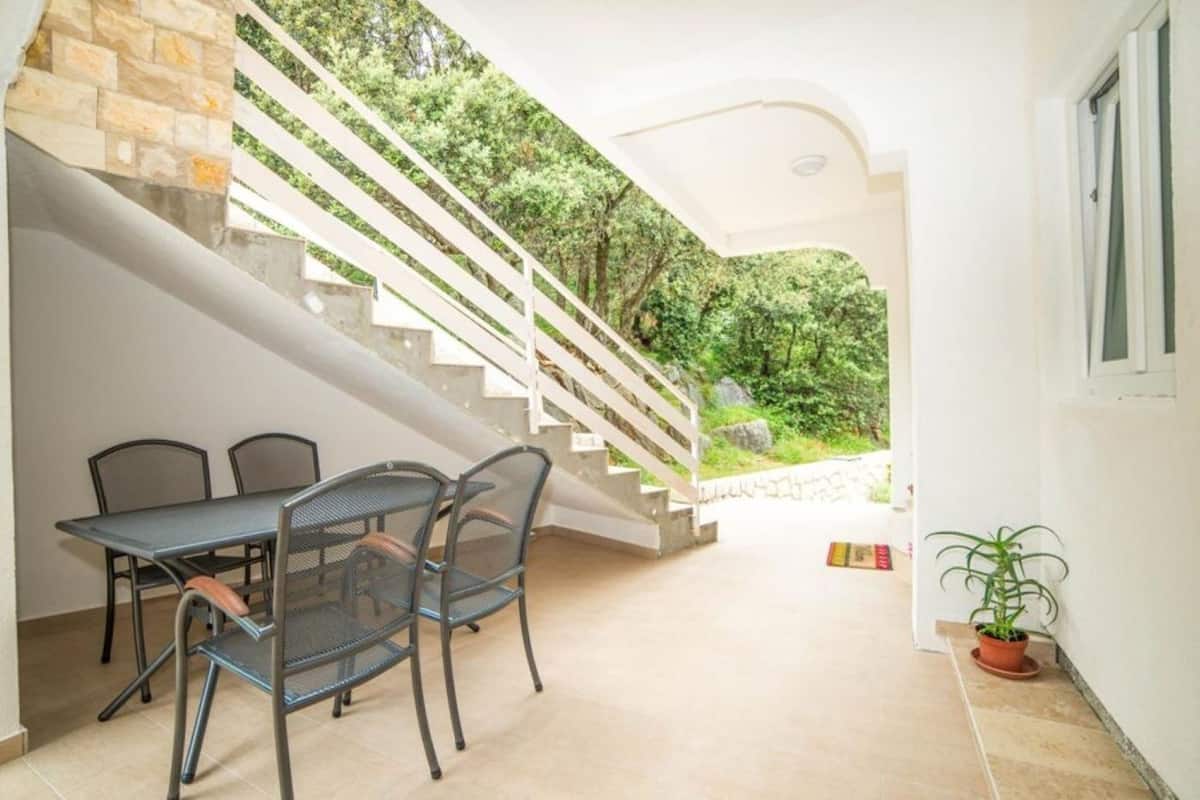 A modern interior with a staircase leading to a balcony, a dining area with a table and chairs, and a potted plant.