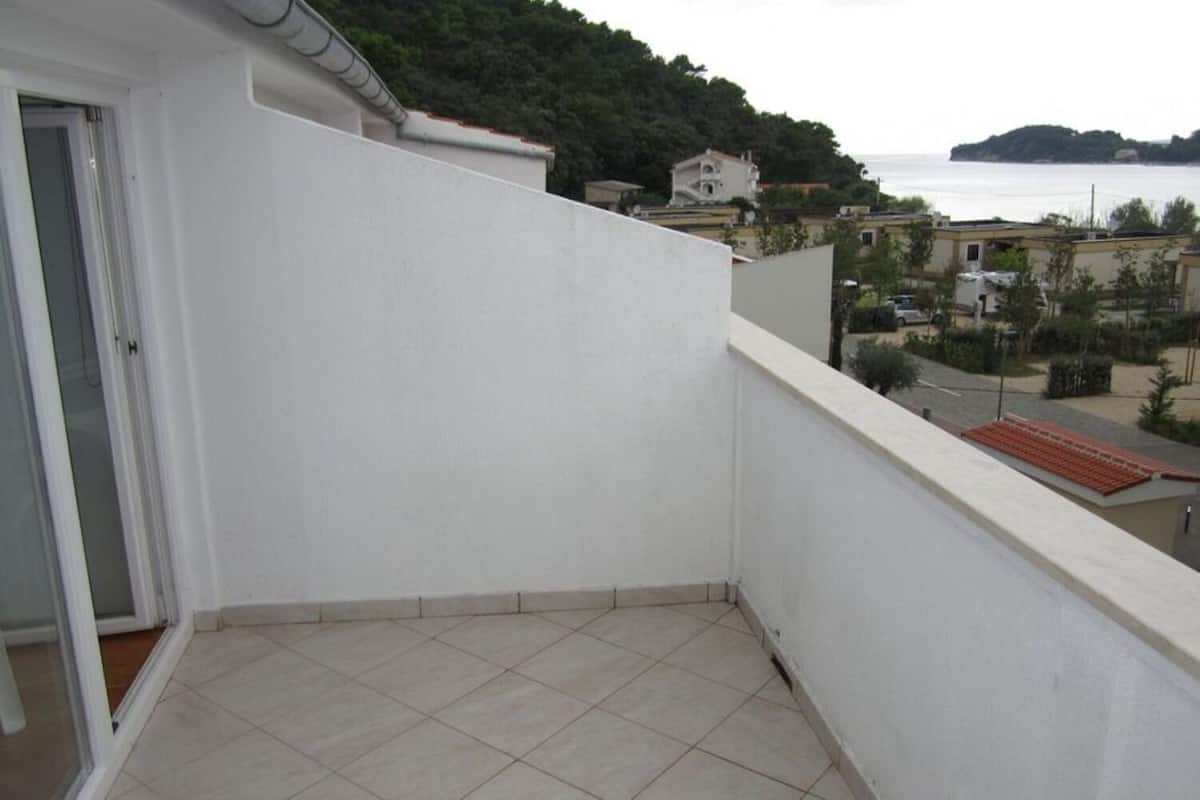 A balcony with a tiled floor, overlooking a residential area and a body of water.