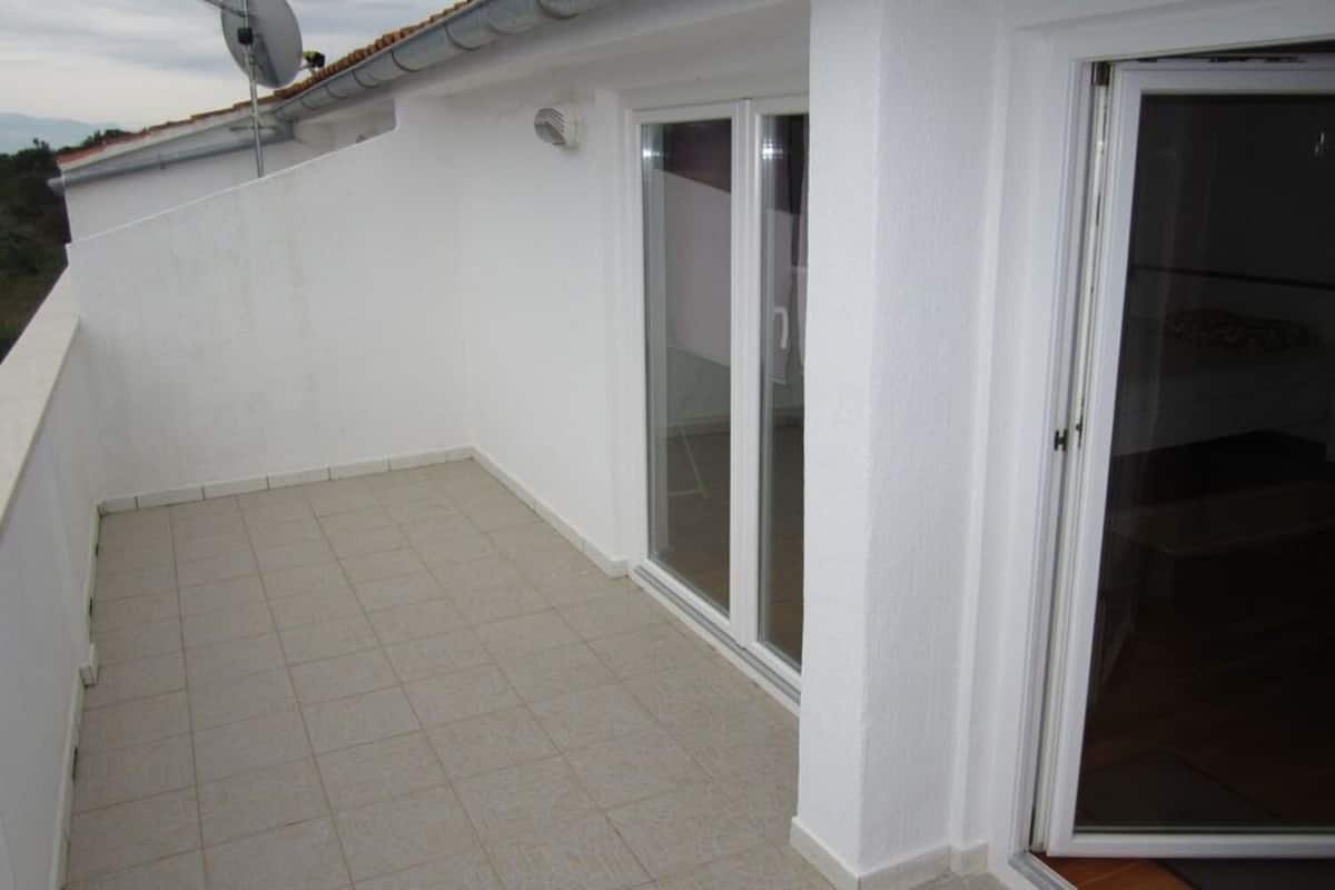 A balcony with tiled flooring, a white wall, and a glass door leading to an interior space.