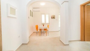 A dining area with a table and chairs, an archway leading to another room, and a wooden door. - Apartments Niki (Rab)