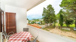 A balcony with a table and chairs, overlooking a coastal area with trees and a road. - Apartments Niki (Rab)