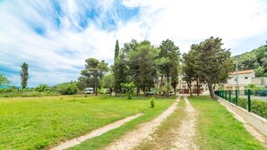 A grassy area with a dirt path leading to a building. - Apartments Niki (Rab)