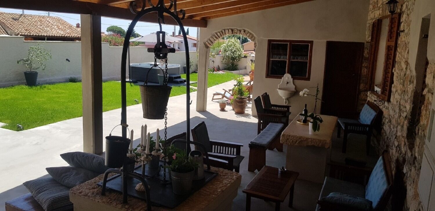 A covered patio with outdoor furniture, a hanging light fixture, and a view of a garden.