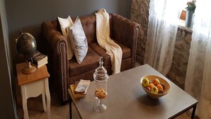 Ein Wohnzimmer mit einem braunen Ledersofa, einem kleinen weißen Beistelltisch, einer Glasdose mit Keksen und einer Obstschale auf einem Couchtisch.