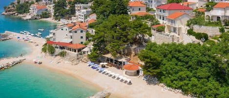 Un pueblo costero con playa, aguas cristalinas y edificios con tejados rojos.