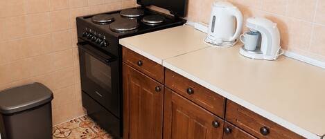 A kitchen with a stove, cabinets, and a trash bin.
