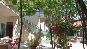 A courtyard with a staircase leading to a balcony, surrounded by potted plants and flowering trees. - Apartment Nera (Vodice)