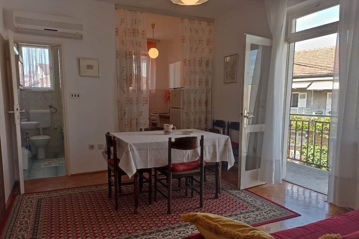 Un coin repas avec une table dressée pour deux personnes, une cuisine en arrière-plan et un balcon doté d’une balustrade.
