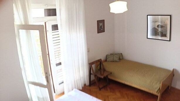 Un dormitorio con una cama grande, un sofá pequeño, una silla de madera y una ventana con cortinas.