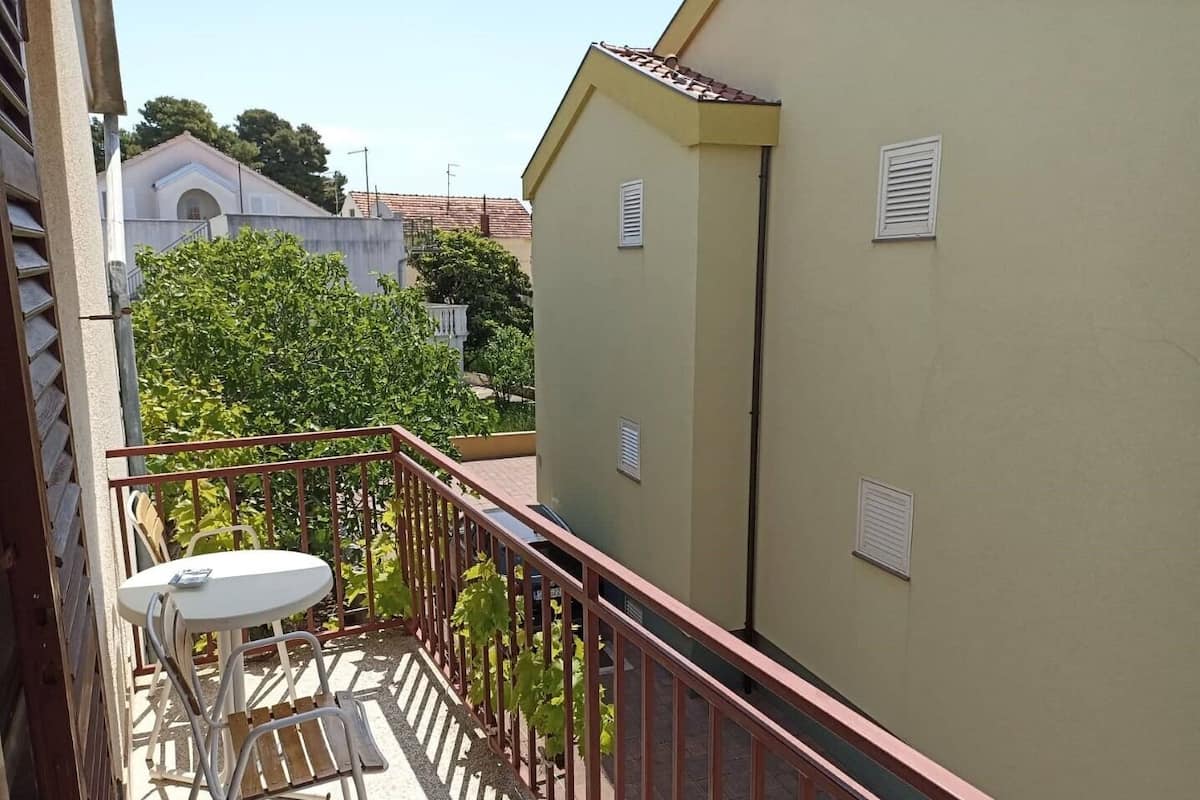 Un balcon avec une table et des chaises, une balustrade, et un bâtiment avec un toit en tuiles en arrière-plan.