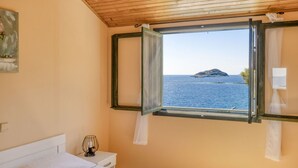 A bedroom with a bed, a bedside table with a lamp, and a window with a view of the sea and a distant island. - House Momento (Blato)