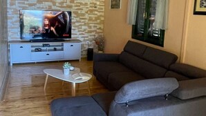 A living room with a grey sofa, a small white table, a TV on a white stand, and a wooden ceiling. - House Momento (Blato)