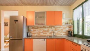 A kitchen with orange cabinets, a stainless steel refrigerator, a dishwasher, a sink, and a stove. - House Momento (Blato)