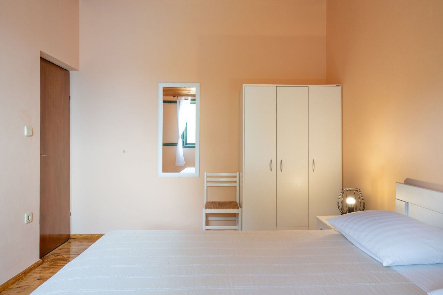 A bedroom with a bed, a wardrobe, a mirror, and a bedside lamp.