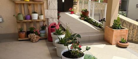 A covered outdoor area with potted plants and a tiled floor.